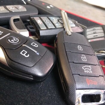 Close-up of several modern car key fobs with buttons for lock, unlock, trunk, and alarm functions on a dark surface.