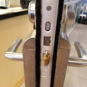 Close-up of a door lock mechanism on a glass door, showing both handles and the lock components in detail.