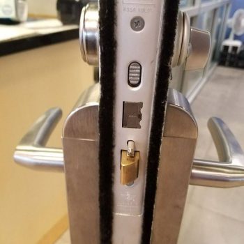 Close-up of a door lock mechanism on a glass door, showing both handles and the lock components in detail.