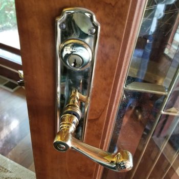 A close-up of a brass door handle and lock set on a wooden door with glass panels.