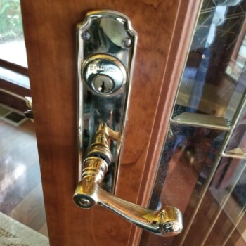 A close-up of a brass door handle and lock set on a wooden door with glass panels.